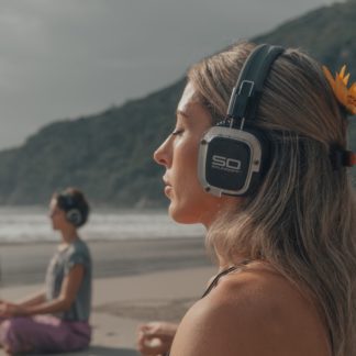 Woman with flower in her hair meditating while wearing Sound Off headphones on a beach